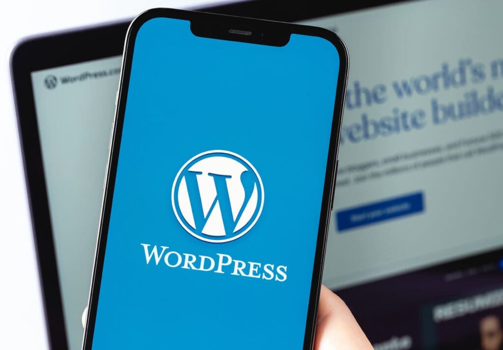 WordPress logo mobile app on screen smartphone iPhone with Macbook closeup. WordPress - open source site content management system. Moscow, Russia - June 22, 2021 Aegisys Wordpress